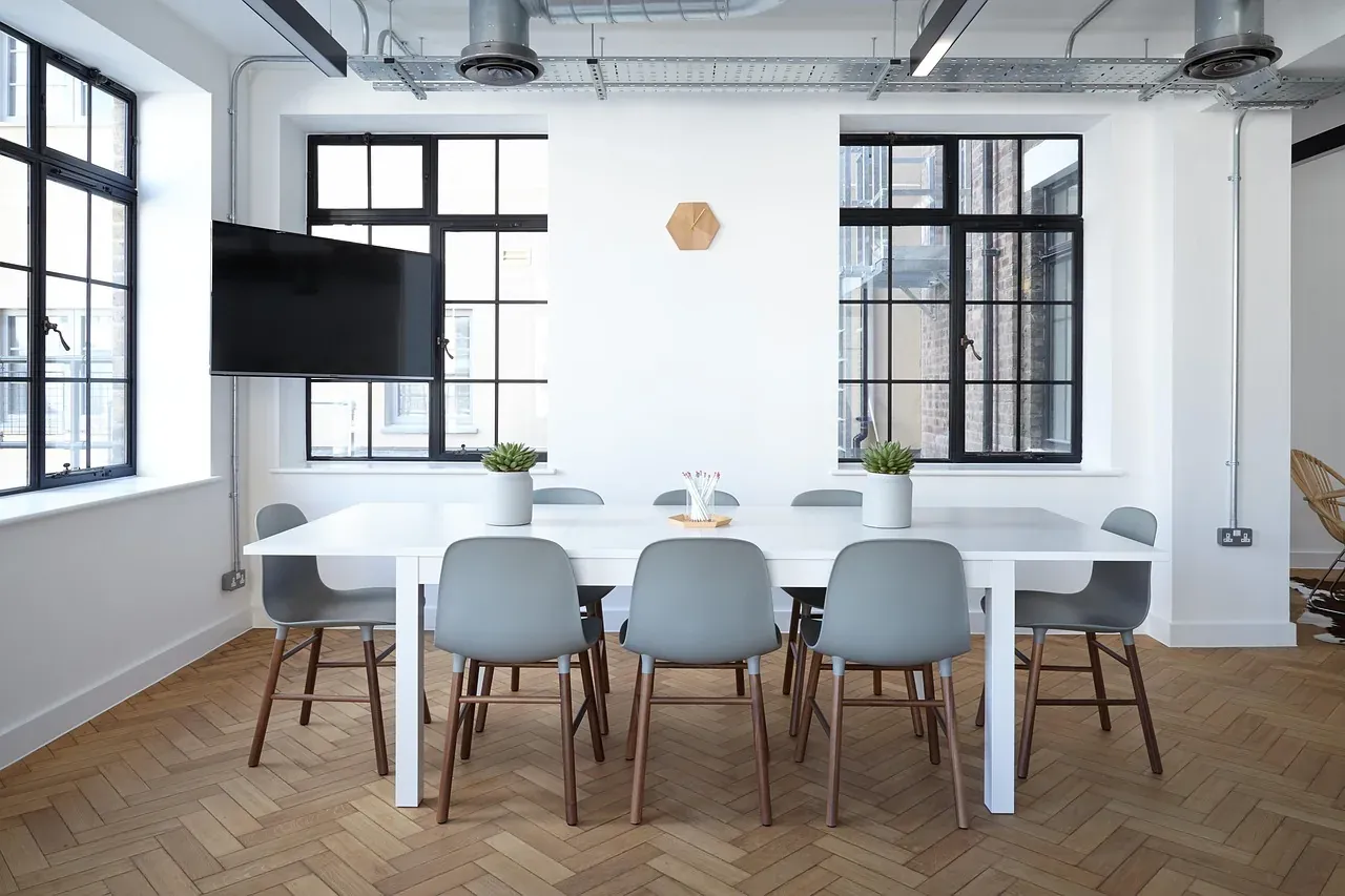 An empty meeting room with a long white table and grey chairs