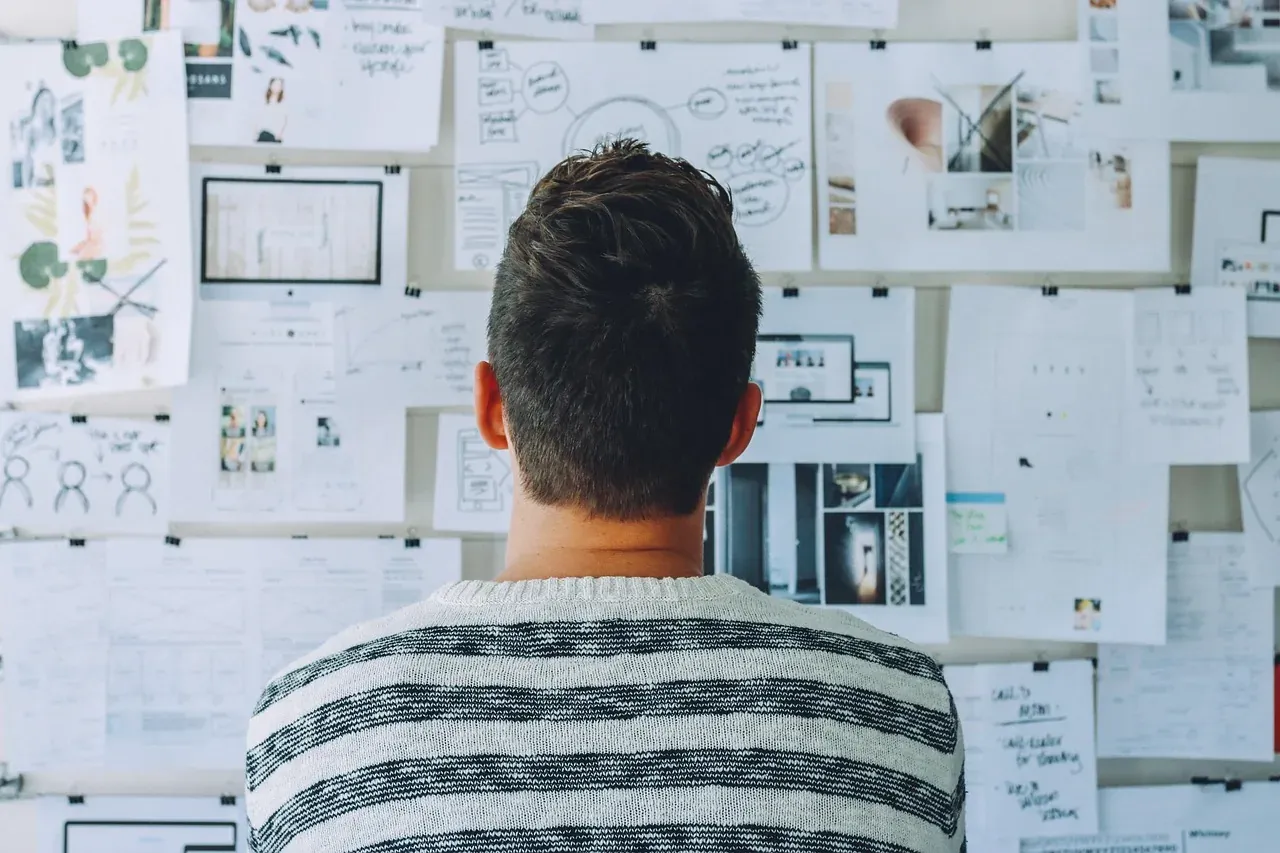 A man studying a wall covered in sketches and notes