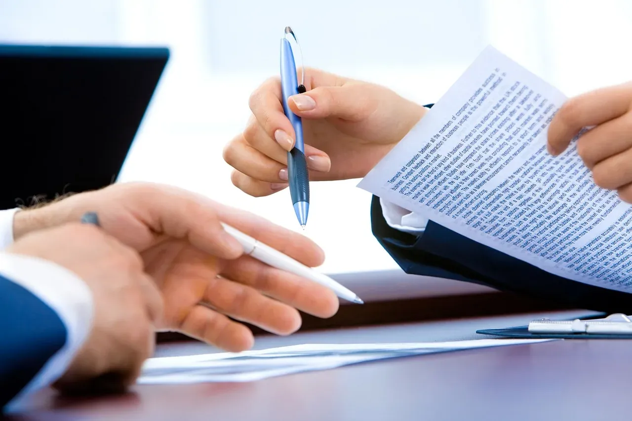 Two people reviewing a printed document with pens in hand