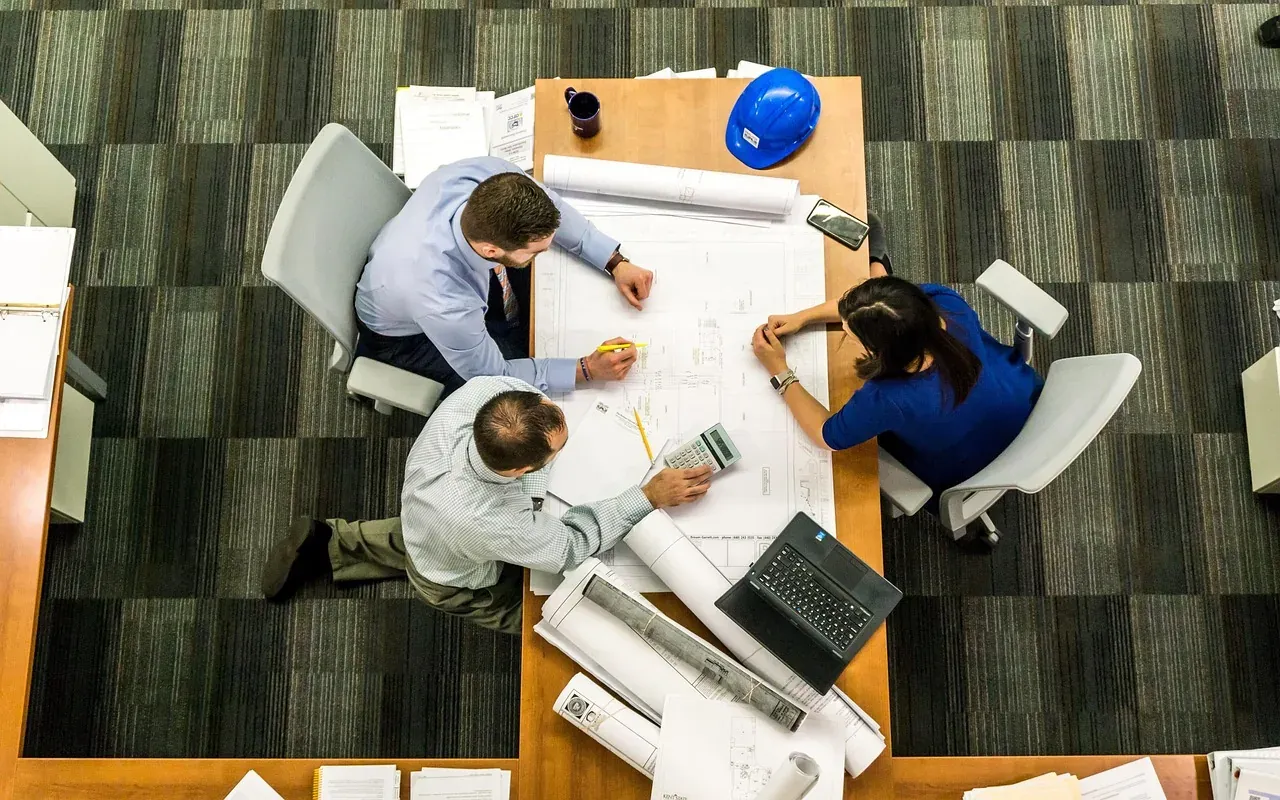 Overhead view of a team meeting over blueprints at a table