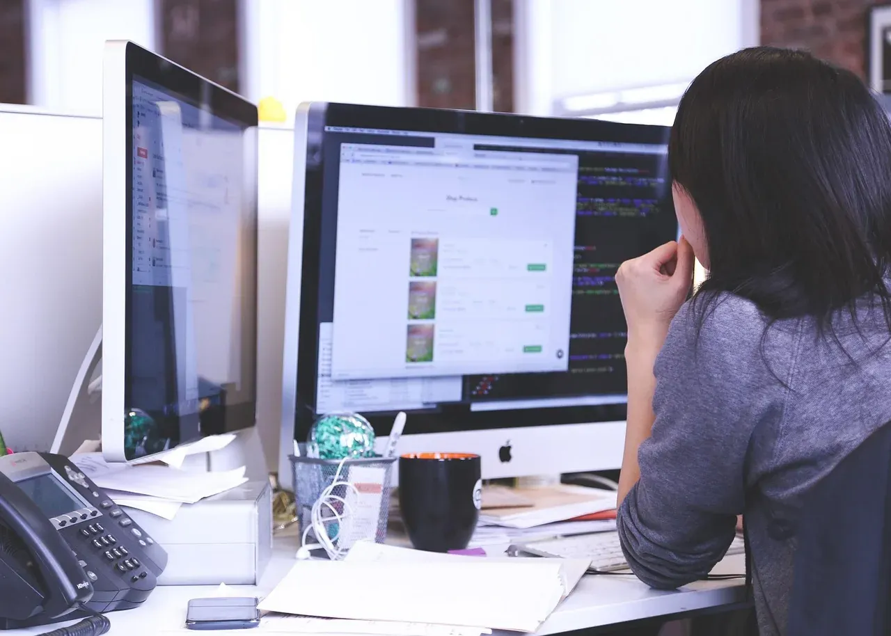 Woman working at a desk with two computer monitors